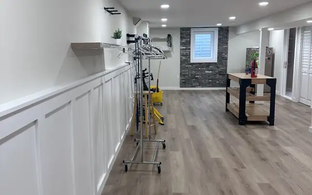 Finished basement in Paramus, NJ with white wainscoting, gray brick accent wall and wood-look plank floor