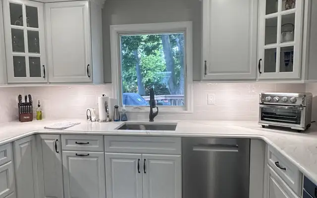 Remodeled kitchen in Paramus, NJ with white raised-panel cabinets, glass-front uppers and a sink under the window