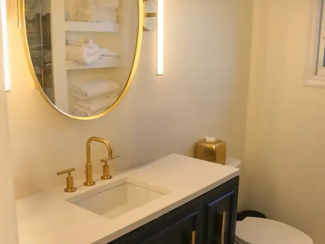 Bathroom vanity with navy cabinet, white quartz top, brass faucet and oval brass mirror