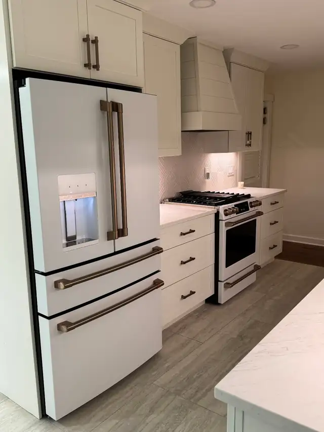 Montclair galley kitchen with white shaker cabinets, a white refrigerator with bronze handles and a panelled range hood