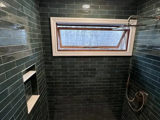 Walk-in shower with dark green subway tile walls, recessed niche and window