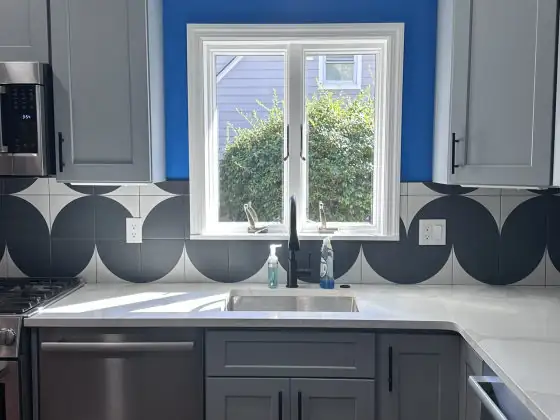 Kitchen with gray cabinets, white quartz countertops and a black-and-white geometric tile backsplash under a blue accent wall